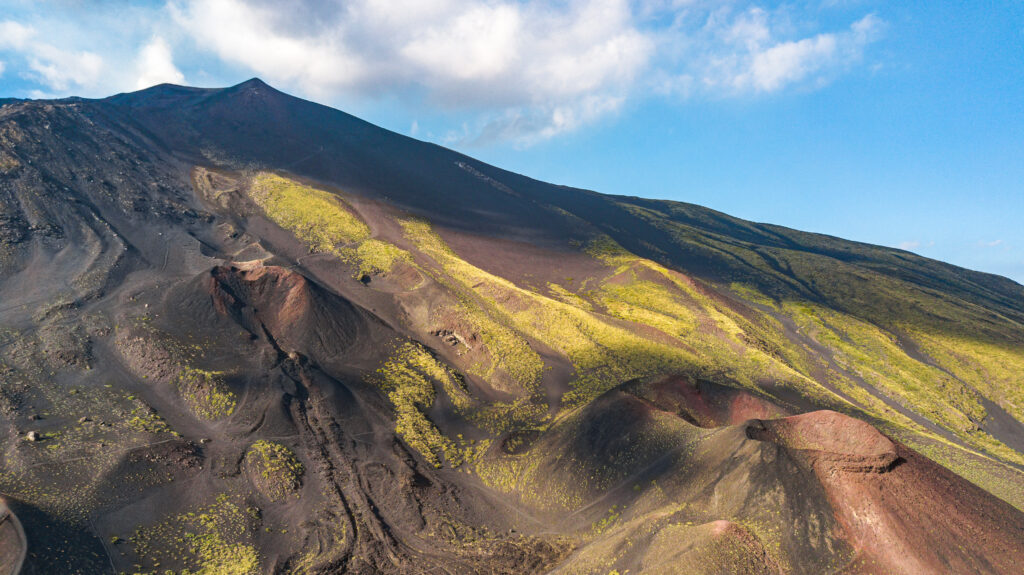 Il paesaggio vulcanico dell’Etna con crateri, colate laviche e vegetazione sulle pendici del vulcano.