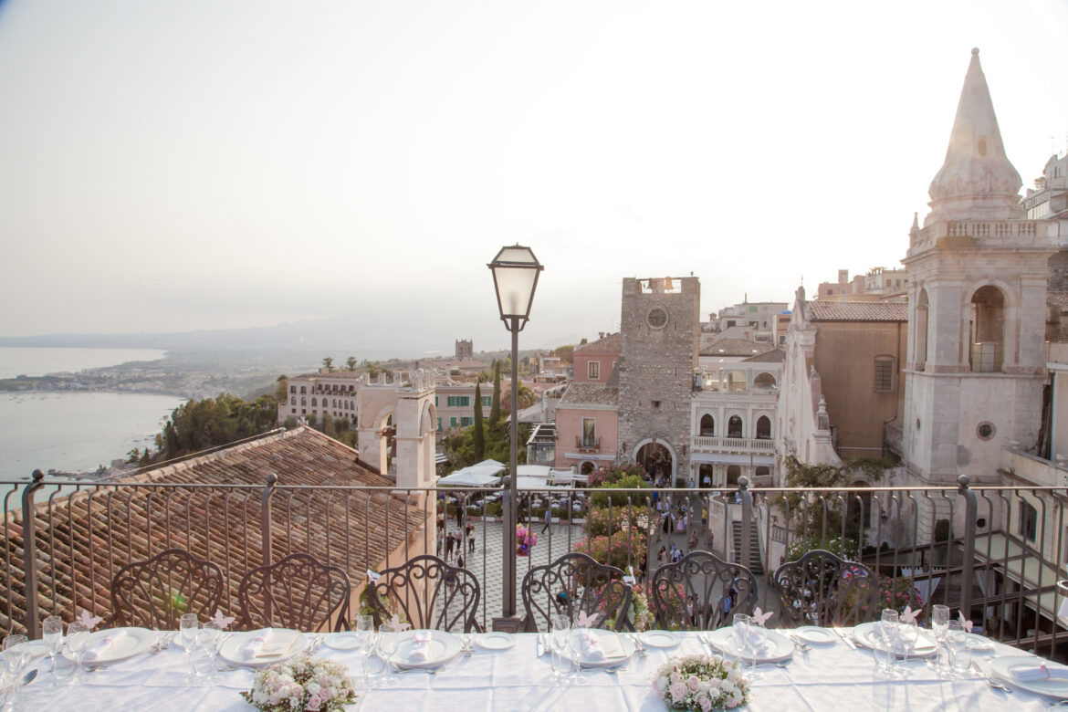 Tavola apparecchiata con vista panoramica su Taormina al tramonto, simbolo della migliore cucina siciliana e dei ristoranti senza glutine dell’isola.