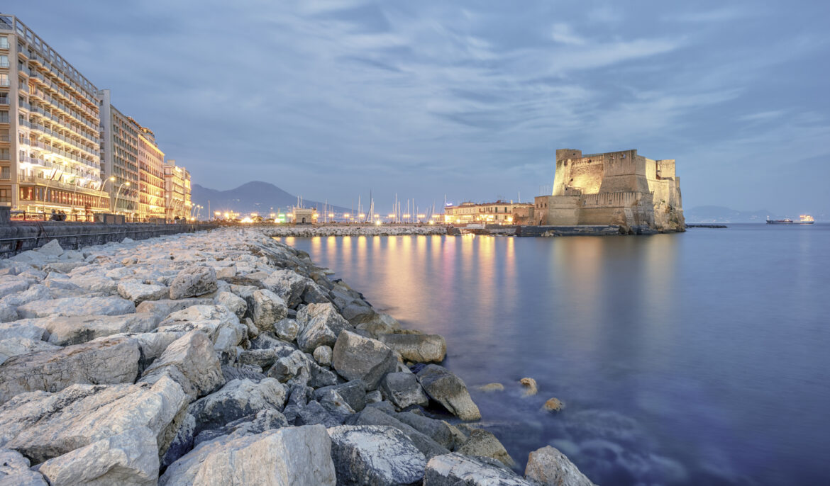 Veduta del Lungomare Caracciolo e di Castel dell’Ovo al tramonto, una delle zone più affascinanti dove soggiornare durante un viaggio a Napoli.