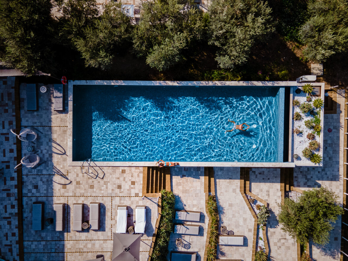 Piscina di un resort di lusso in Sicilia immerso nella natura mediterranea, vista dall’alto.