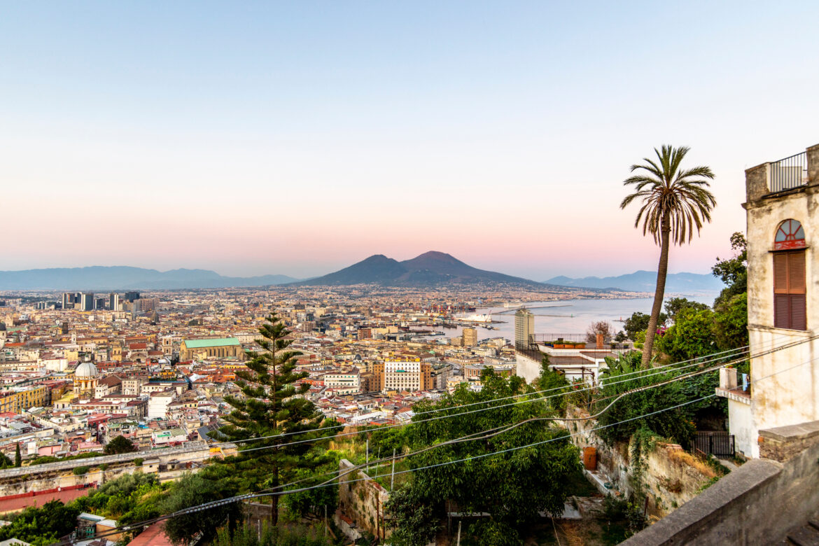 Panorama di Napoli al tramonto con il Vesuvio sullo sfondo, immagine di copertina della guida Glutentrip dedicata ai migliori ristoranti e pizzerie senza glutine della città.