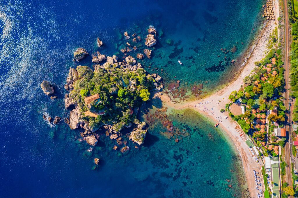 Veduta aerea di Isola Bella a Taormina, con il mare cristallino e la sottile lingua di sabbia che collega l’isolotto alla costa siciliana.