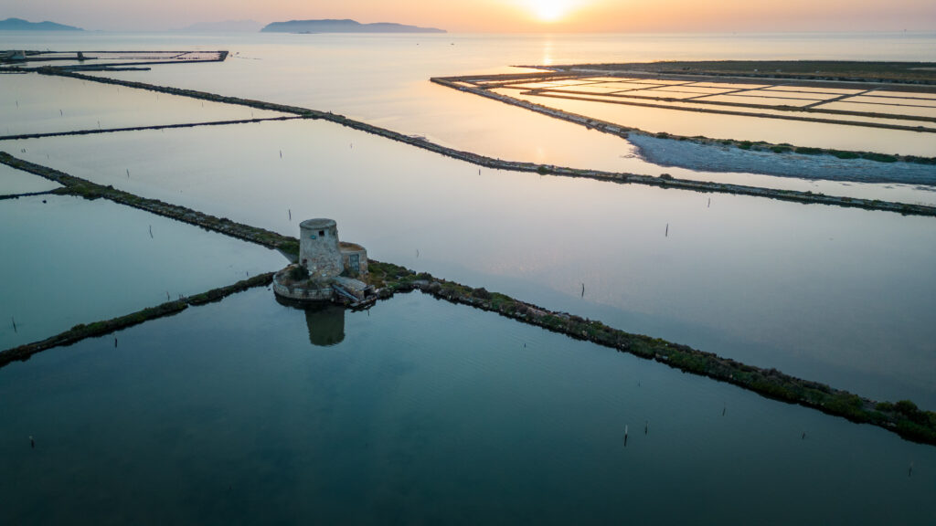 Veduta aerea delle saline di Trapani al tramonto, con le vasche di evaporazione e l’antico mulino a vento sulla costa della Sicilia occidentale.