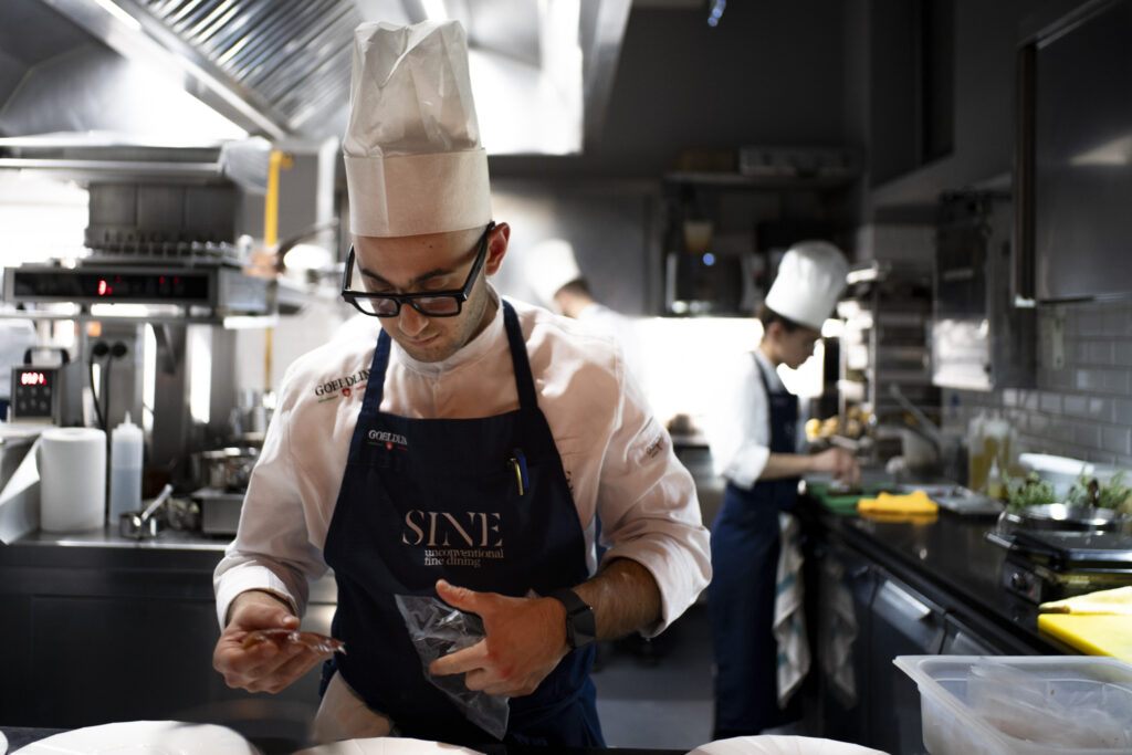 Uno chef della brigata di SINE by Di Pinto al lavoro durante la Kitchen Experience, esperienza esclusiva nel ristorante stellato Michelin di Milano con attenzione al senza glutine.