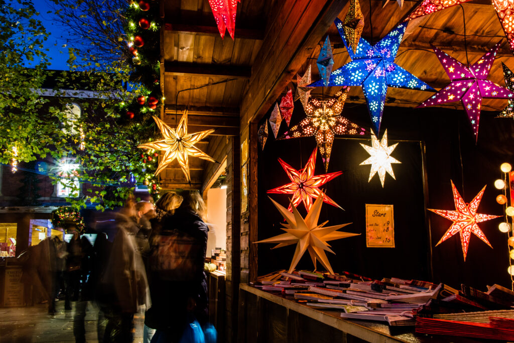 Stelle natalizie colorate e illuminate esposte in una bancarella di legno durante un mercatino di Natale
