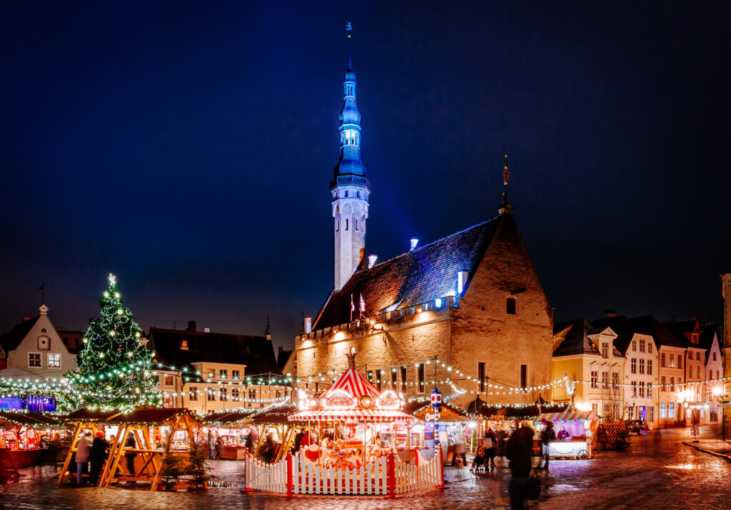 Mercatino di Natale nella Piazza del Municipio di Tallinn con albero illuminato, giostra e bancarelle davanti al municipio medievale