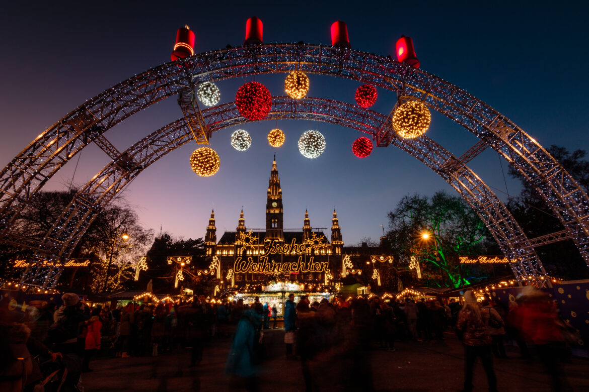 Ingresso illuminato del mercatino di Natale di Vienna a Rathausplatz con decorazioni luminose e Municipio sullo sfondo