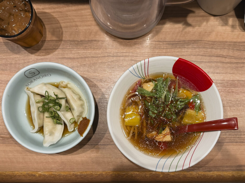 Ciotola di ramen giapponese con brodo, noodles e verdure, accompagnata da gyoza nel ristorante Soranoiro di Tokyo.