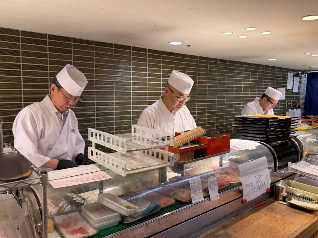 Tre chef giapponesi preparano sushi dietro il bancone di un ristorante tradizionale.