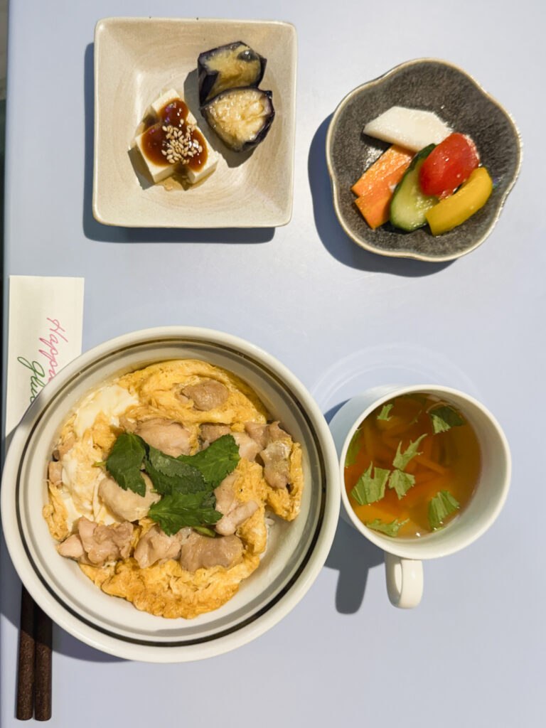 Oyakodon con riso, pollo e uova, accompagnato da zuppa, tofu, melanzane e verdure in piccoli piatti giapponesi.