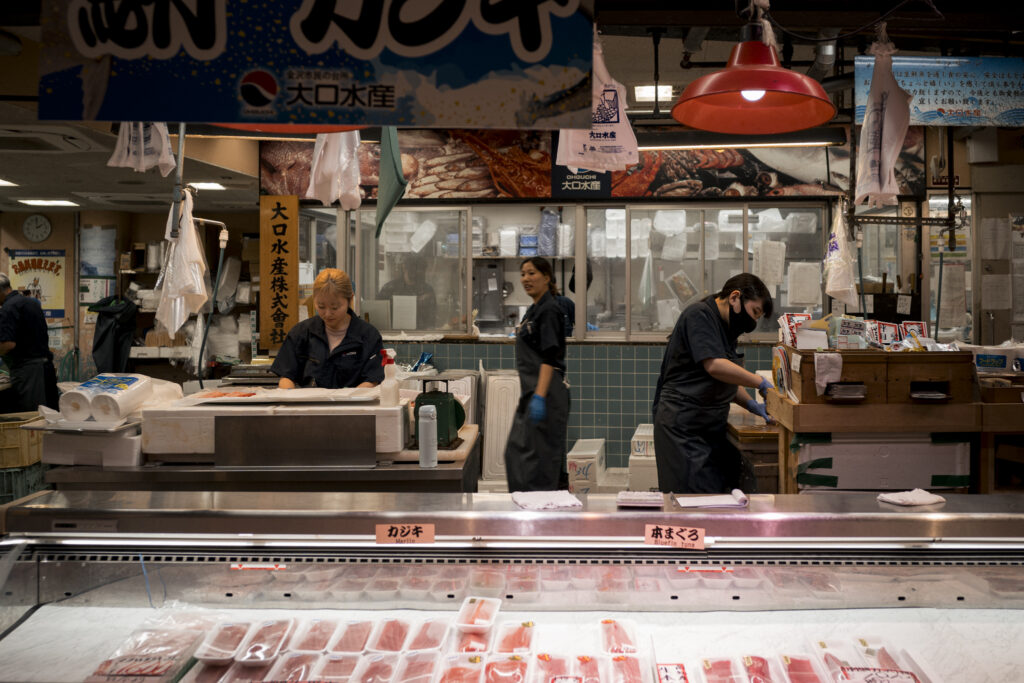 Tre addette lavorano dietro il banco di un mercato del pesce giapponese, con filetti di tonno esposti nella vetrina refrigerata.