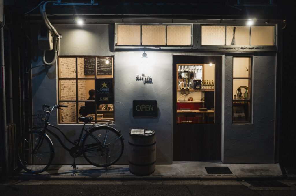 Facciata illuminata di un piccolo ristorante a Kyoto di sera, con una bicicletta parcheggiata all’ingresso.